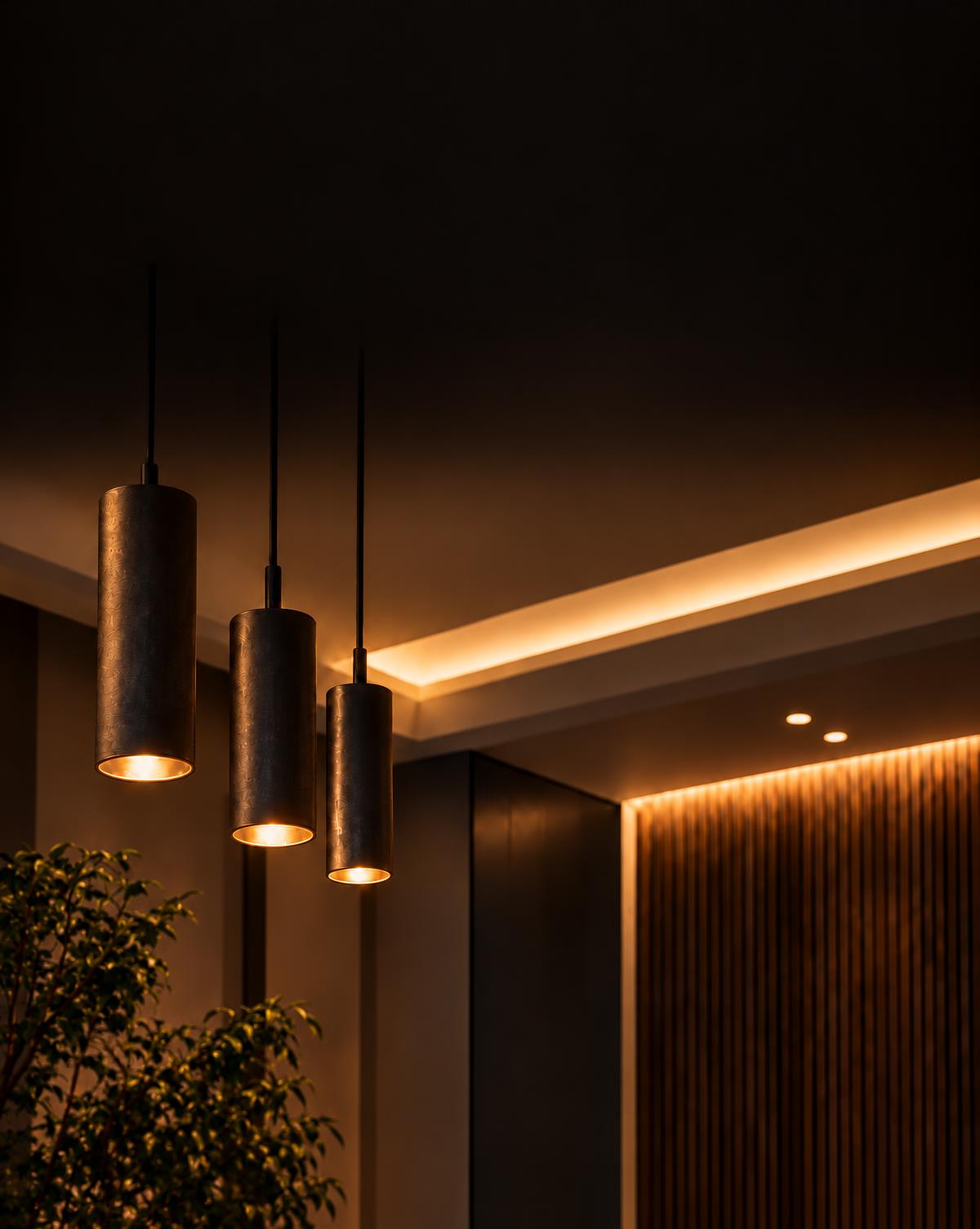 Bronze cylinder pendants glowing warm over a cove-lit ceiling and wood slat wall